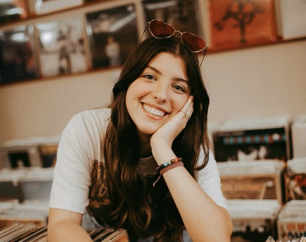 young woman leans over smiling with hand on face in a record store