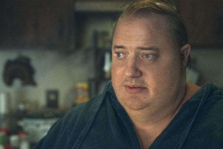 White man in dark blue sweatshirt gazes off camera with a kitchen in the background