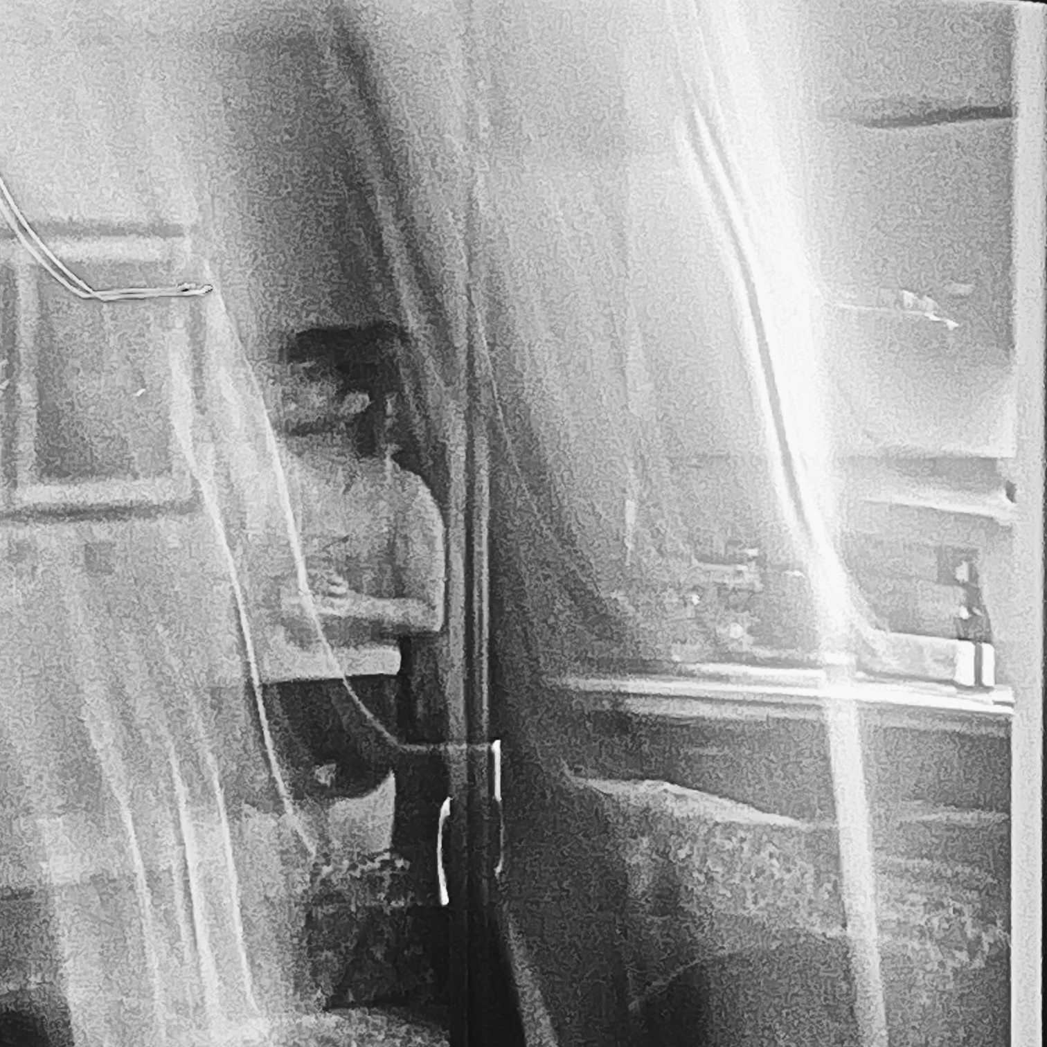 A photograph of a man in an apartment; a curtain covers the scene.