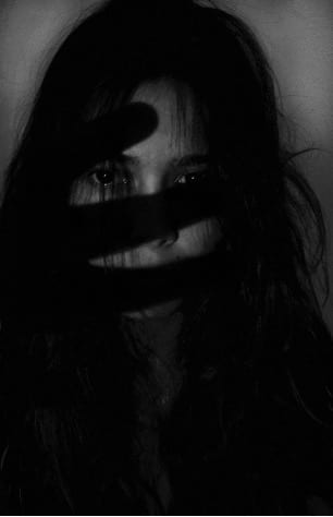 A person sits in darkness, their face obscured and missing